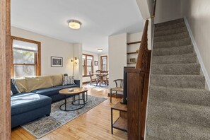 Uma sala de estar com sofá, mesa de centro e tapete, uma escada e uma área de jantar com cadeiras e mesa.