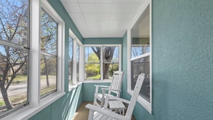 Une véranda aux murs de couleur turquoise, dotée de grandes fenêtres et de chaises Adirondack blanches.