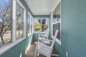 Een zonruimte met teal muren, grote ramen en witte Adirondack stoelen.