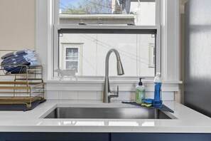 Een keuken met een rvs spoelbak, een raam met uitzicht op gebouwen, een zeepdispenser en een metalen rek met opgevouwen handdoeken.