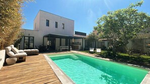 A modern house with a swimming pool, wooden deck, and outdoor furniture.