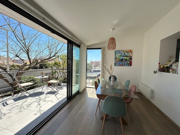 A modern dining area with a glass table, chairs, and a view of the outdoors.