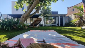 Um pátio com manta, cadeira e mesa, com um livro e uma cesta.