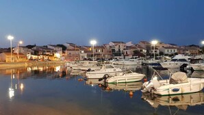 Uma marina com barcos atracados, superfície de água calma e edifícios ao fundo.