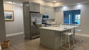 A modern kitchen with a stainless steel refrigerator, a microwave, and a sink with bar stools.