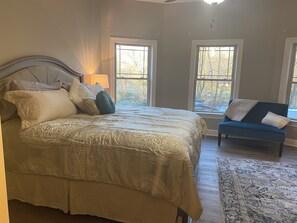 Ein Schlafzimmer mit einem großen Bett, zwei Fenstern, einem blauen Sofa und einem Teppich.