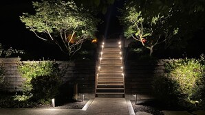 A nighttime outdoor staircase with steps leading up to a building, surrounded by greenery and illuminated by lights.