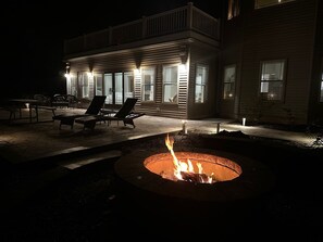 Uma casa com lareira em primeiro plano, área de estar externa e um pátio bem iluminado à noite.