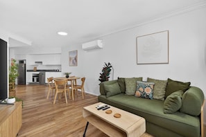 Ein modernes Wohnzimmer mit einem grünen Sofa, einem Holztisch und einem Essbereich mit Tisch und Stühlen.