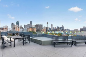 Eine Dachterrasse mit Sitzgelegenheiten im Freien, Blick auf eine Stadtlandschaft und einem klaren Himmel.