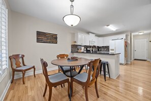 Un coin repas avec une table ronde et quatre chaises, une cuisine avec des meubles blancs et un luminaire au plafond.