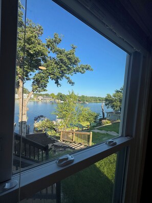 A view through a window of a lake with trees and a wooden deck.