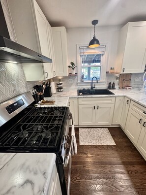A modern kitchen with white cabinets, a stainless steel stove, and a wooden floor.
