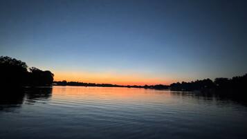 A calm lake at dusk with a clear horizon and trees silhouetted against the sky.