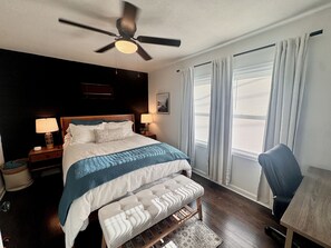 A hotel room with a bed, bedside tables, a ceiling fan, a chair, and a window with curtains.