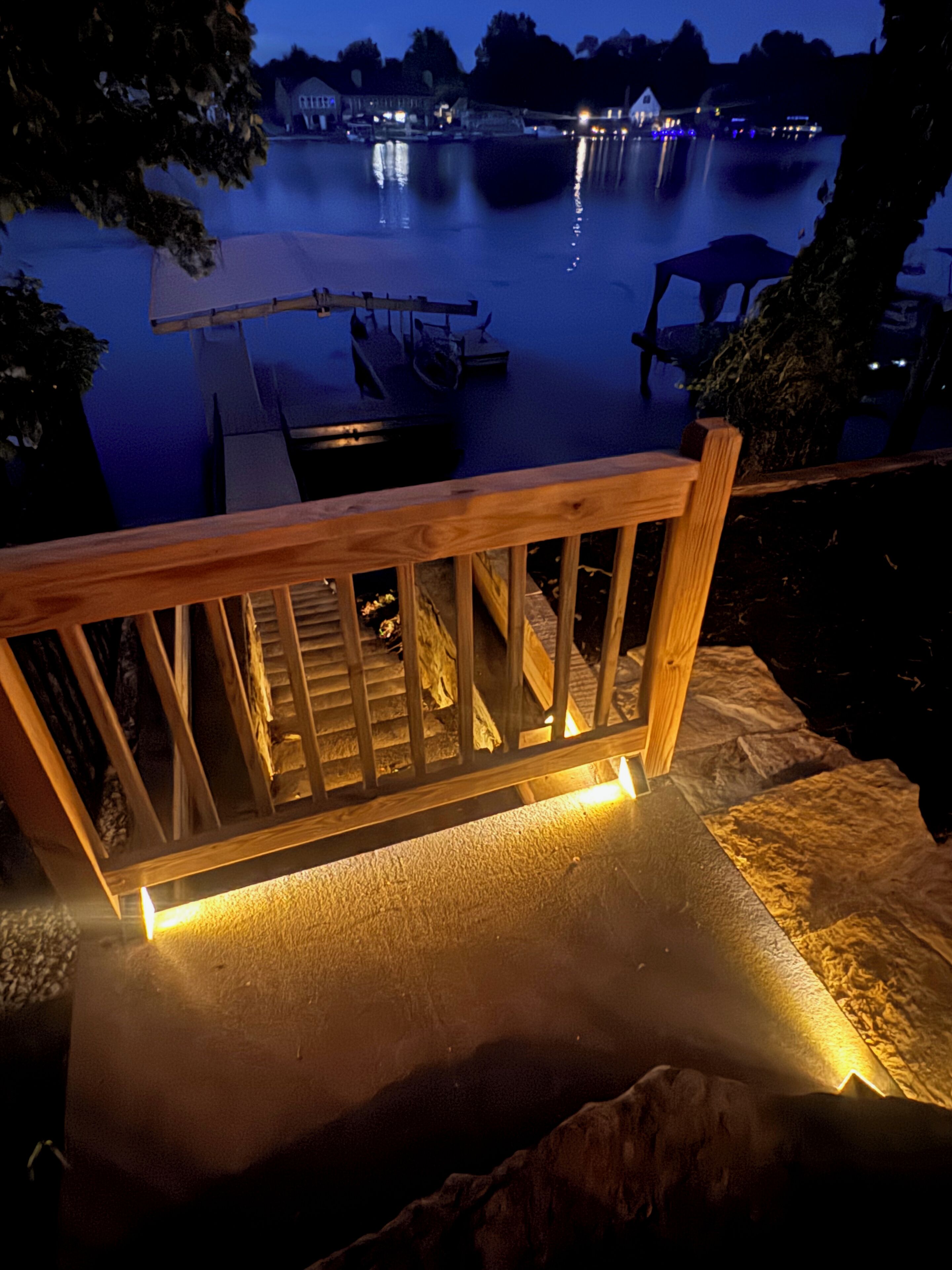 Una terraza de madera con barandilla que da a un cuerpo de agua tranquilo de noche.