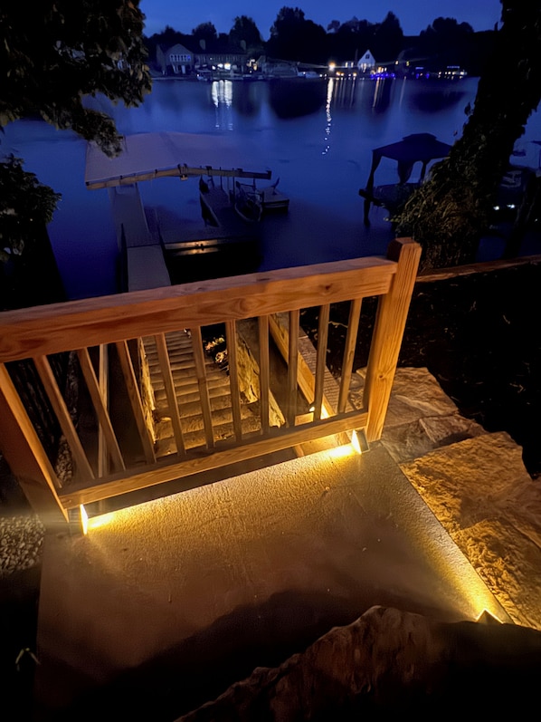 A wooden deck with a railing overlooking a calm body of water at night.