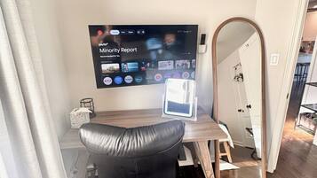 Moderni huone, jossa on seinälle asennettu televisio, jolta näkyy elokuva »Minority Report», musta toimistotuoli, puinen työpöytä ja lattiasta kattoon ulottuva peili.