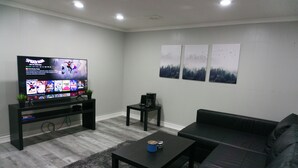A living room with a flat-screen TV, a black sofa, a coffee table, and a small side table. - Modern 3 Bedroom Guest Suite (Toronto)