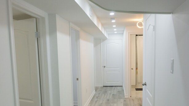 A hallway with white walls and a light wood floor, leading to a door at the end. - Modern 3 Bedroom Guest Suite (Toronto)