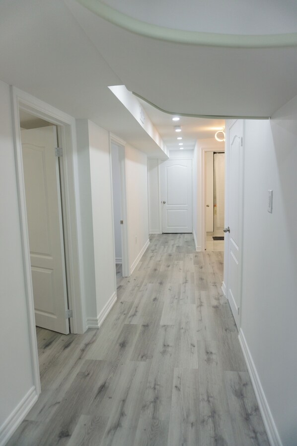 Un couloir aux murs blancs et au plancher en bois clair, qui mène à une porte au fond.