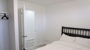 A bedroom with a bed, a door leading to another room, and a coat rack. - Modern 3 Bedroom Guest Suite (Toronto)