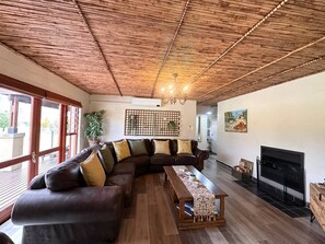 Ein Wohnzimmer mit Holzboden, einem Ecksofa, einem Couchtisch aus Holz, einem Kamin und einem großen Fenster.