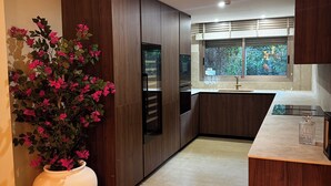 Uma cozinha moderna com armários de madeira escura, um vaso grande branco com flores cor-de-rosa e uma janela com vista para o verde.