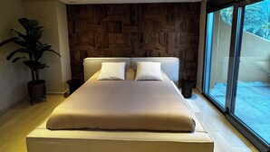 Quarto moderno com uma cama grande, parede de pedra e vista através de uma janela ampla.
