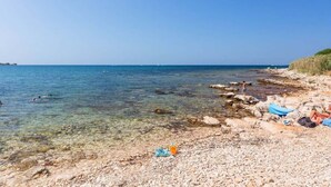 Ein kiesiger Strand mit klarem Wasser, einige badende Personen und eine felsige Küste.