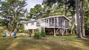 A two-story house with a porch and a deck, surrounded by trees. - Pearl in the Pines – Bikes, Kayaks, EV Charger, Screened Porch, Fire Pit, Pets (Chincoteague)
