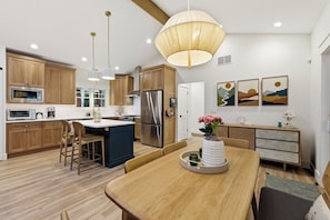 Eine moderne Küche mit Holzausstattung, Edelstahlgeräten, einem Essbereich mit Holztisch und Pendelleuchten.