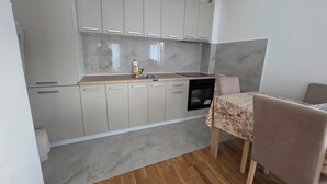 A kitchen with grey cabinets, a built-in oven, and a dining area with a table and chairs. - Urban Comfort Apartments, Podgorica (Podgorica)