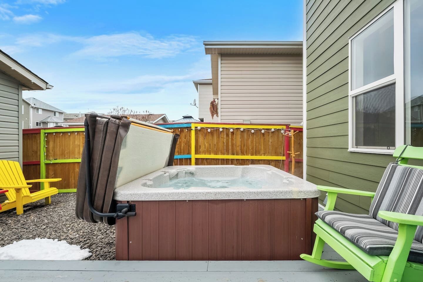Een achtertuin met een jacuzzi, een houten schutting en een groene stoel.