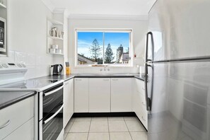 Une cuisine moderne avec des meubles blancs, un réfrigérateur en acier inoxydable et une fenêtre donnant sur des arbres et des immeubles.