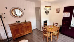 En matplats med ett träbord och stolar, ett träskåp, en spegel och en hängande lampa.