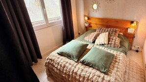 Ett sovrum med en sänggavel i trä, två sänglampor, en säng med ett mjukt täcke och ett fönster med gardiner.
