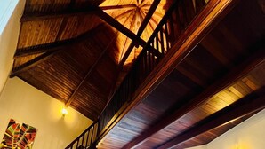 Uma sala ampla com um sofá amarelo, escada de madeira e cozinha ao fundo.