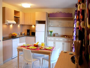 A compact kitchen with modern appliances, a dining table set for two, and a small refrigerator. - Sunny Coastal Escape in Saint-cyprien (Saint-Cyprien)