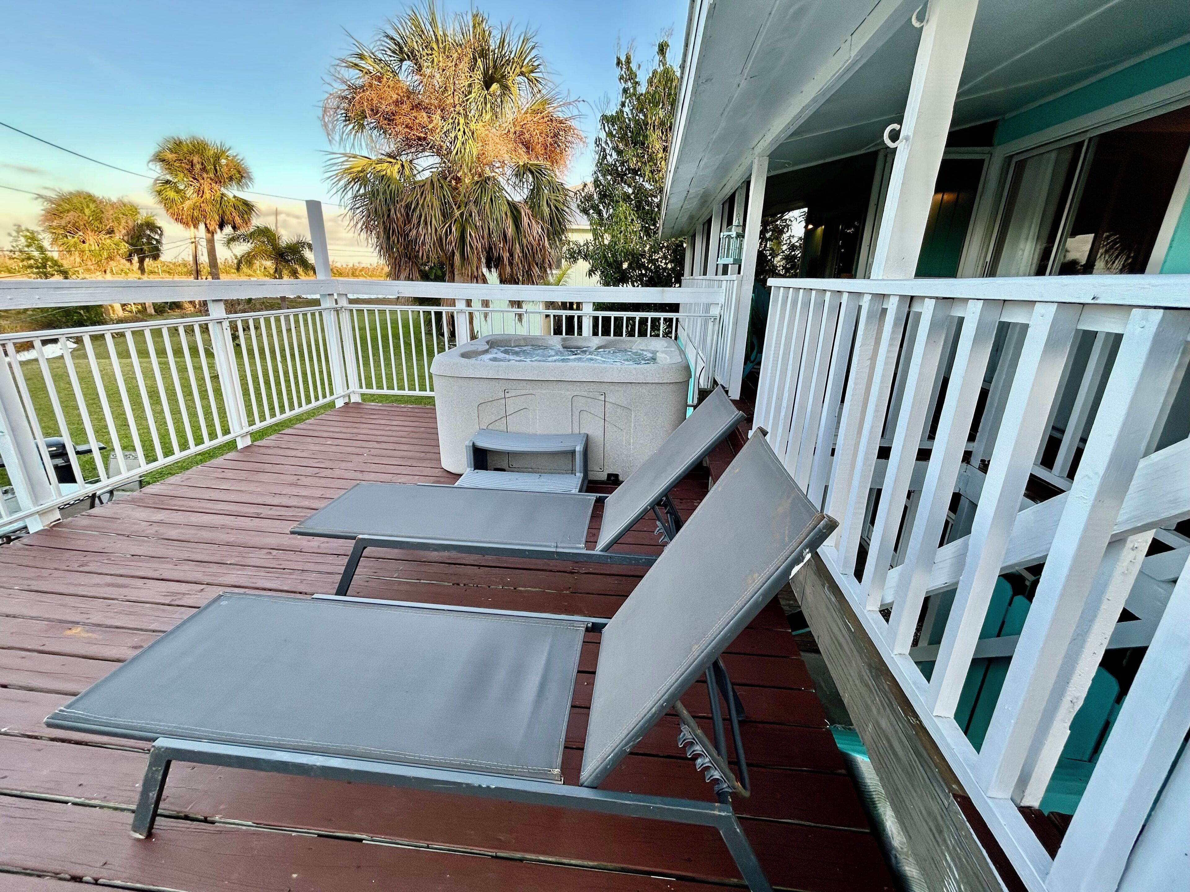 Een houten terras met twee loungestoelen, een whirlpool en een witte balustrade.