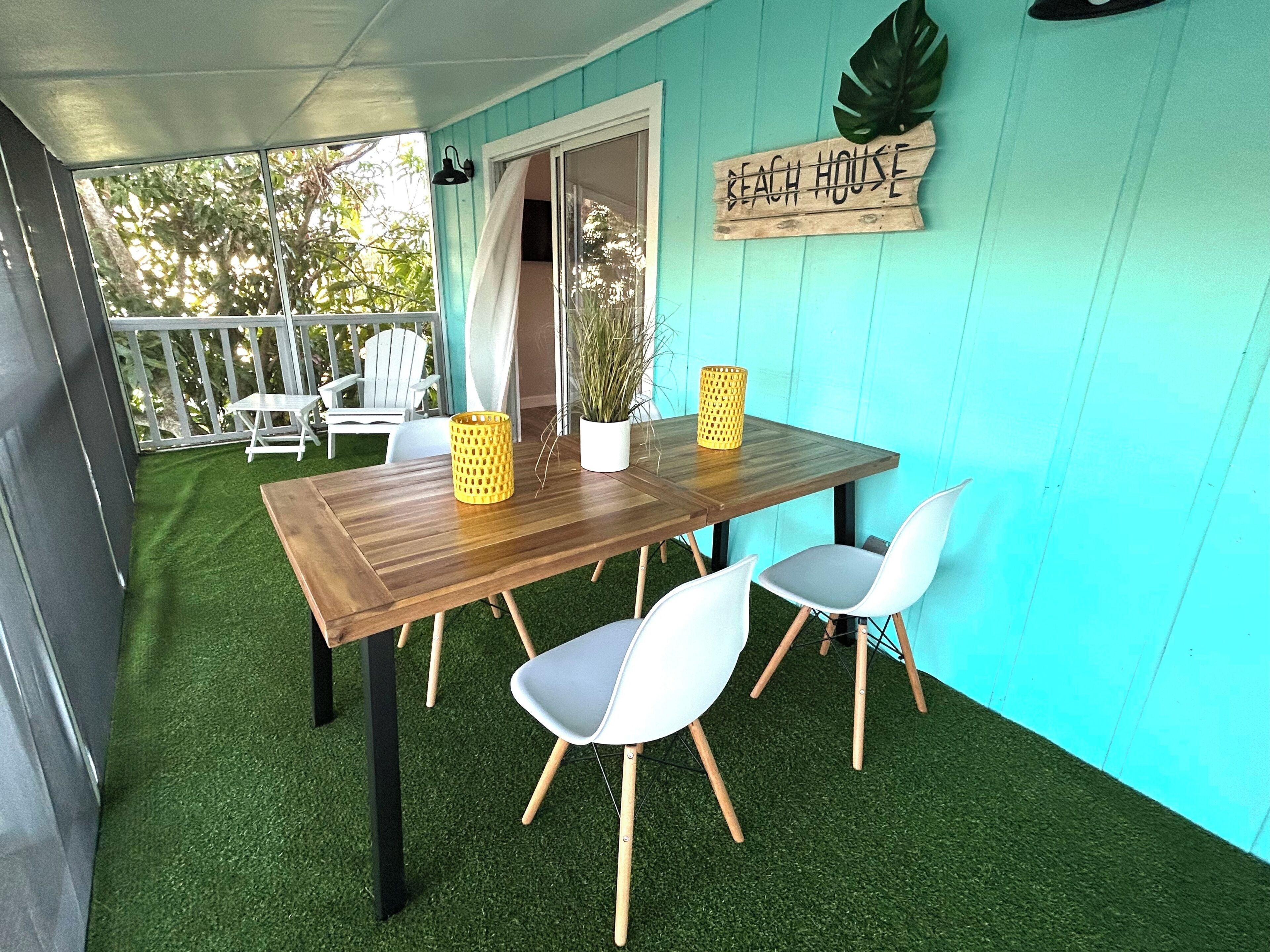 A wooden table with chairs, a potted plant, and a sign reading 'Beach House' on a teal wall.