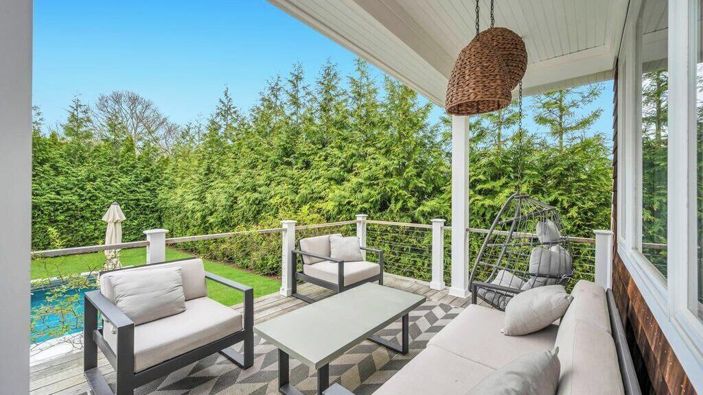 A covered outdoor seating area with a pool view, a hanging light fixture, and a wooden railing.