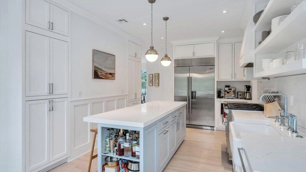 A modern kitchen with white cabinetry, a central island, stainless steel appliances, pendant lighting, and a view into the dining area.