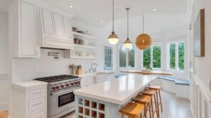 A modern kitchen with white cabinetry, a central island with stools, a stove, and pendant lighting. - Exquisite Shinnecock Hills Classic, Private Yard featuring Heated Pool,... (Southampton)