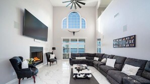A spacious living room with a fireplace, a large flat-screen TV, a sectional sofa, and a large window with a view. - Lakefront Estate Sleeps 18, Bunk & Game Room & Boat House w/Swim Hole & Kitchen! (Pittsburg)