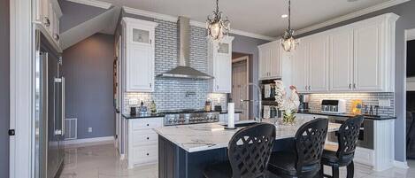 A modern kitchen with white cabinetry, a central island, and black chairs.