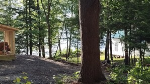 Uma área arborizada com uma estrutura de madeira, possivelmente uma cabana ou abrigo pequeno, próxima a um corpo d'água.