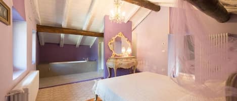 A bedroom with a wooden ceiling, a chandelier, a bed with a white bedspread, a vanity with a mirror, and a window.