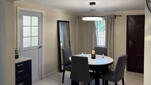 A dining area with a round table, four chairs, a ceiling light, and a door. - Stay Exchange Modern Chill Retreat w/ Private Backyard Oasis (Ocho Rios)