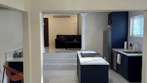 A modern living room with a sofa, a dining area with a table, and a kitchen with a window. - Stay Exchange Modern Chill Retreat w/ Private Backyard Oasis (Ocho Rios)